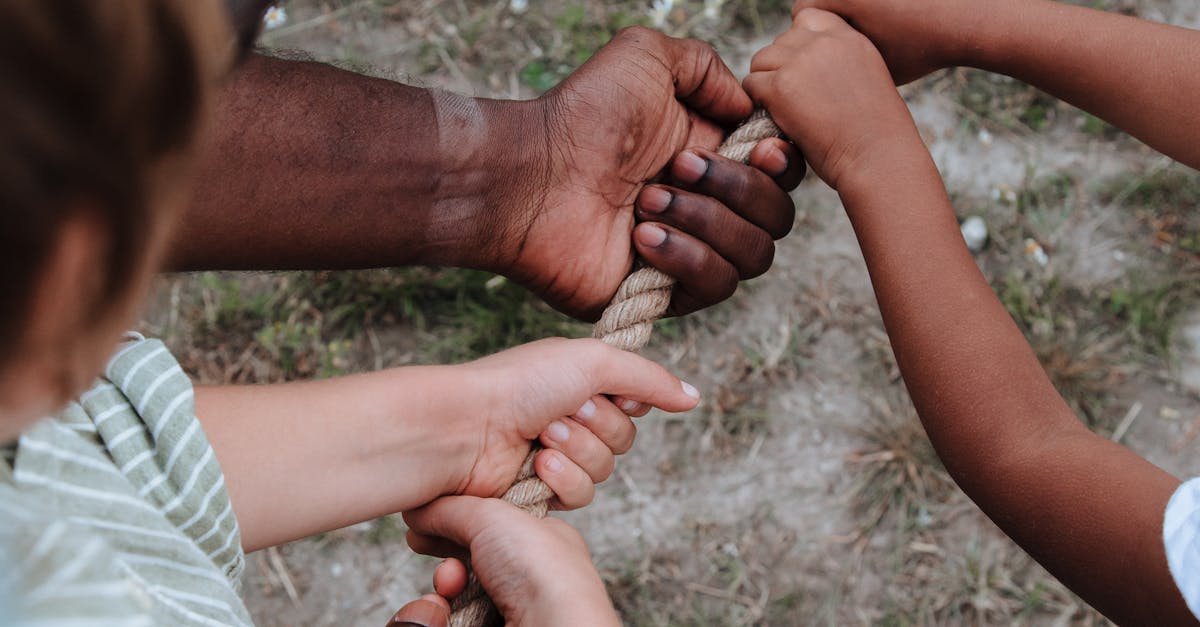 Hands of diverse people tugging on a rope outdoors, symbolizing teamwork and unity.